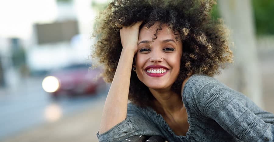 young-black-woman-with-curly-hair-looking-directly-at-you-while-smiling
