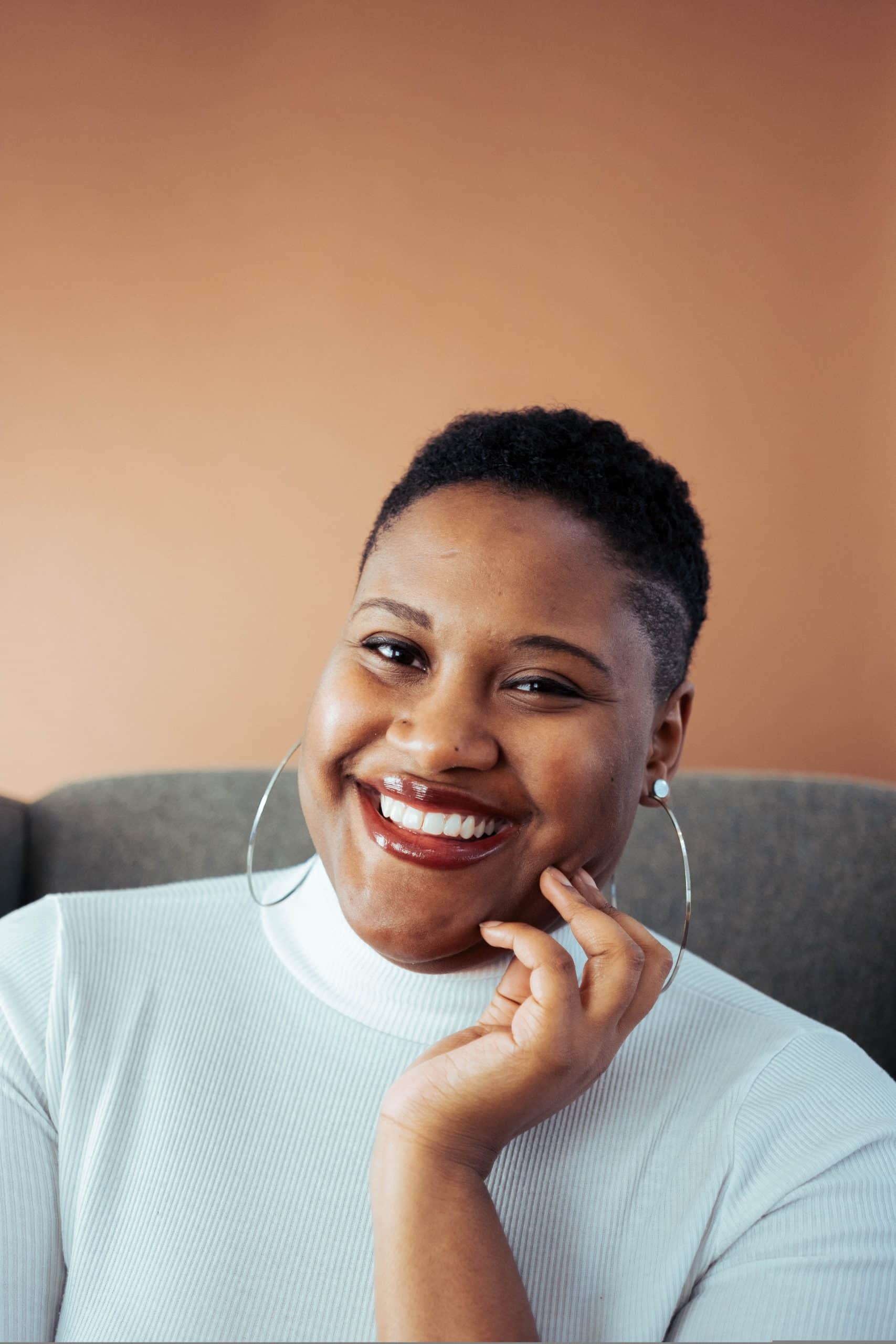 middle-aged-black-woman-with-short-hair-sitting-on-the-couch-smiling-directly-towards-the-camera